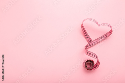 Фотография Heart shape created from rolled out measure tape on light pink table background