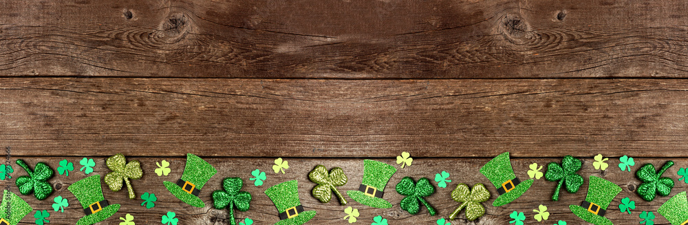 St Patricks Day shamrock and leprechaun hat bottom border. Top down view over a rustic wood banner background with copy space.