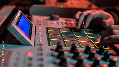 The hands of an artist creating music with his drum machines under red light.
