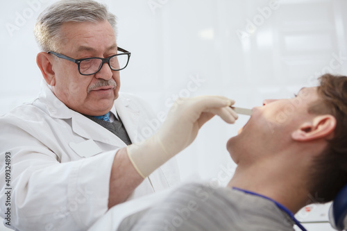 Close up of a senior male dentist examining teeth of a patient
