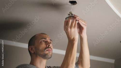 A young man is repairing a ceiling soffit. Replacing the LED lamp at the downlight photo