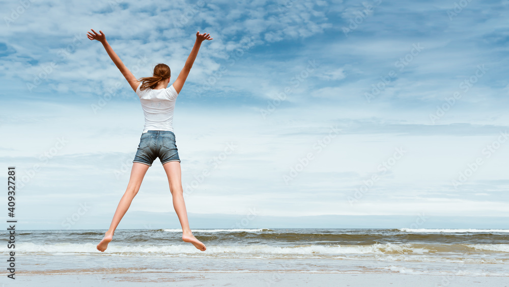 Obraz premium Happy girl jumping on the beach at day time- against blue sky