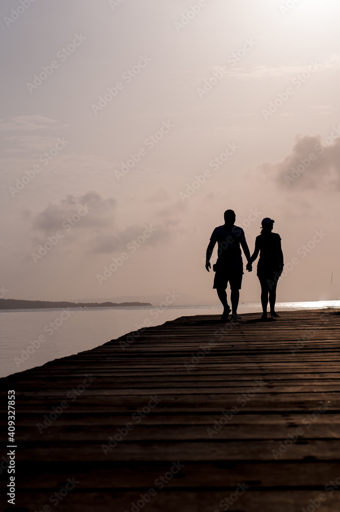 Vertical back view of a couple silhouette walking hand in hand along a ...