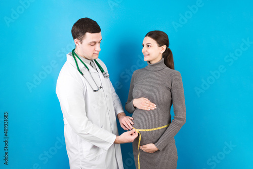 happy beautiful pregnant young woman touching her bare tummy while a doctor is measuring it photo