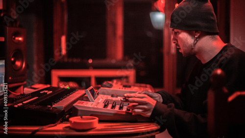 A producer in his studio, creating beats with his drum machines. Under red lights. 