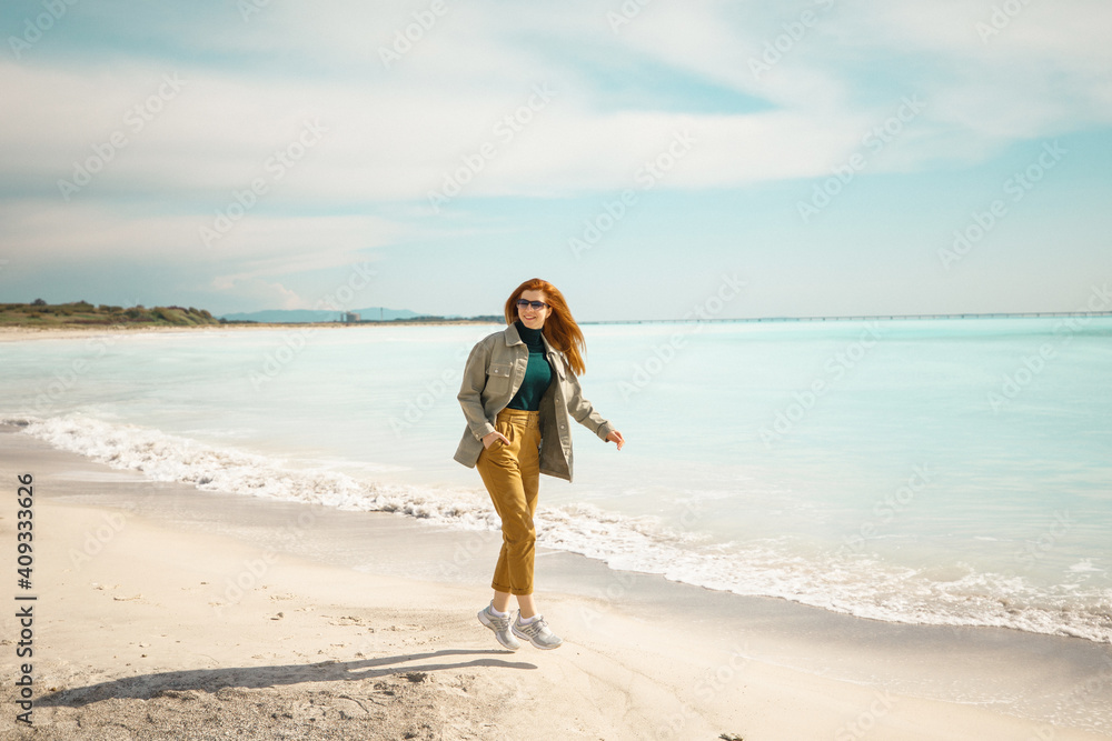 young beautiful red-haired girl walking on the beach near the ocean young beautiful red-haired girl walking on the beach near the ocean