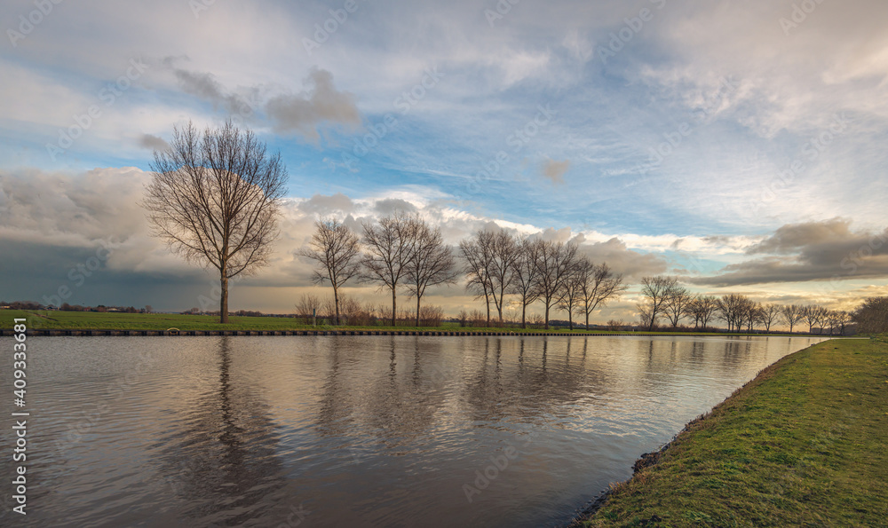 Bare trees in a row along a canal. The silhouettes contrast against the cloudy sky. It is winter in the Netherlands. Bare trees in a row along a canal. The silhouettes contrast against the cloudy sky. It is winter in the Netherlands.