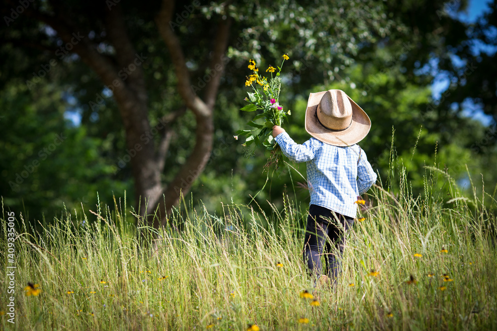 Little boy with cowboy hat in the field of grass and flowers, holding a  flower bouquet he made by himself in his hand. Stock Photo | Adobe Stock