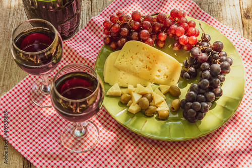 Two glasses of red wine with a bunch of grapes, cheese and olives.