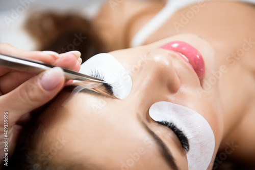 Beautiful young woman during eyelash extension in a salon.