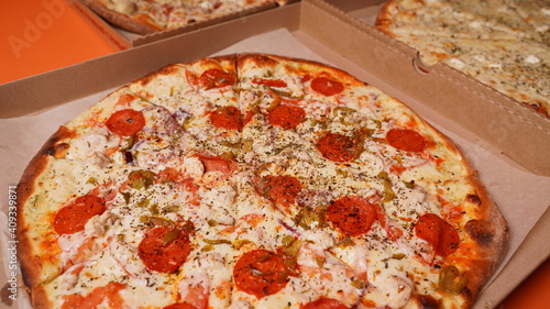 Close up of large pizzas in box on orange background. Appetizing pizzas with different ingredients