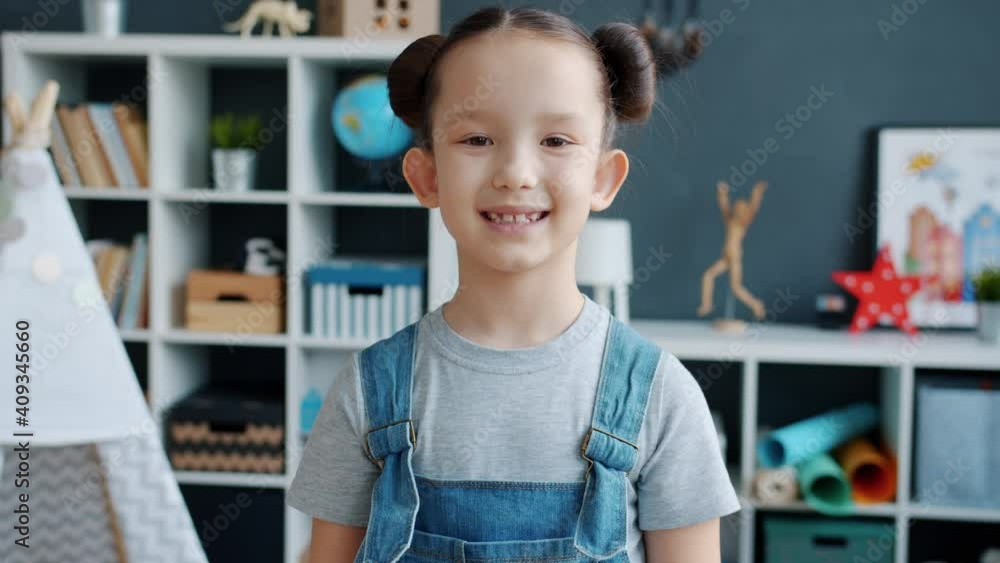 Adorable kid wearing casual clothing is smiling looking at camera standing alone in apartment. Happy childhood and cheerful children concept.
