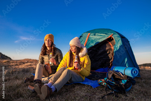 Portrait of two young women sitting and enjoying a mountain sunset next to their tent.