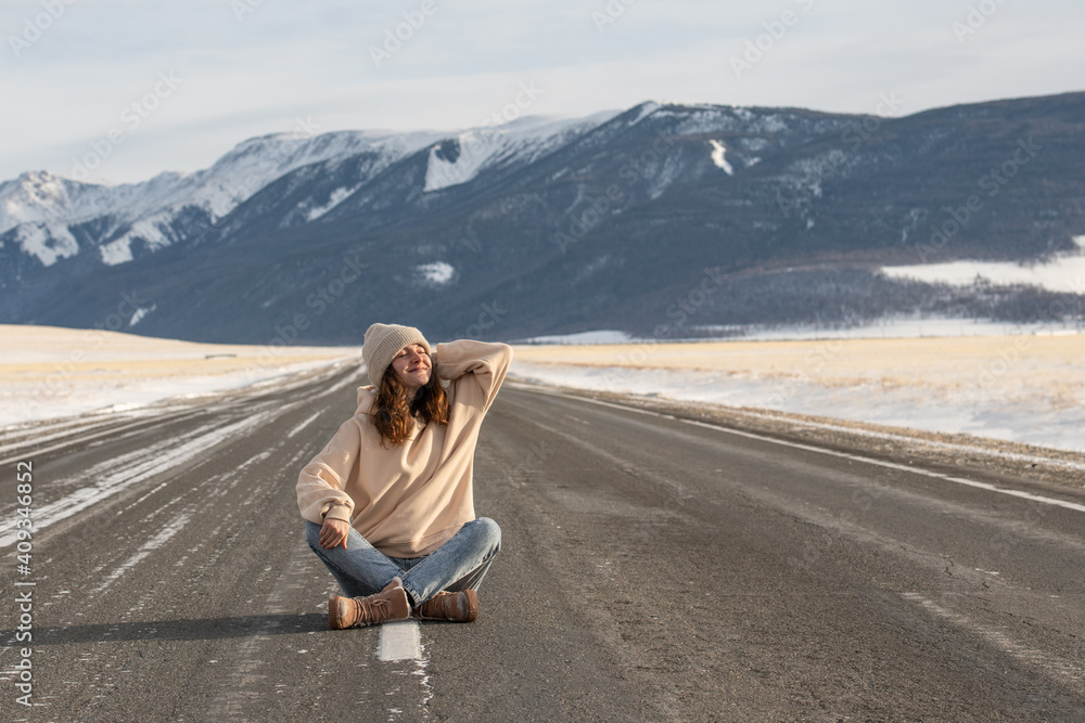 Young caucasian woman sitting on empty road against mountains on background