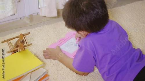 Happy Asian klid little boy preschool writing at the magnetic drawing board at home on carpet. Funny child playing magnetic drawing board. Education Learning to draw concept. Back view photo