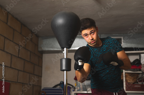 Young caucasian man boxing with a boxing bag at the garage	
