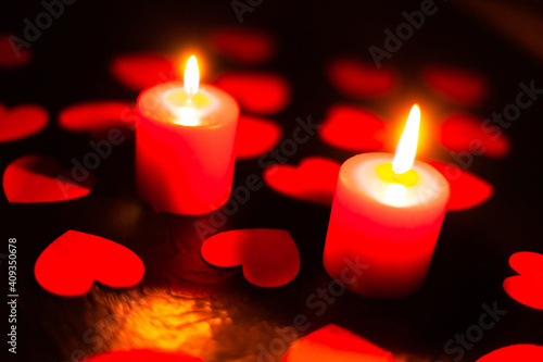 two red burning candles on a black textured background  around lie red hearts with blurry background  used as a background or texture  soft focus