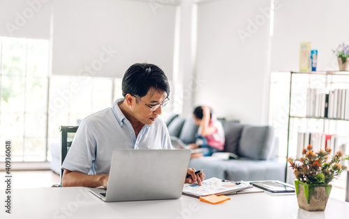 Smiling asian man relaxing using laptop computer working and video conference meeting chat with his girl daughter learning reading book and studying knowledge at home.work from home concept