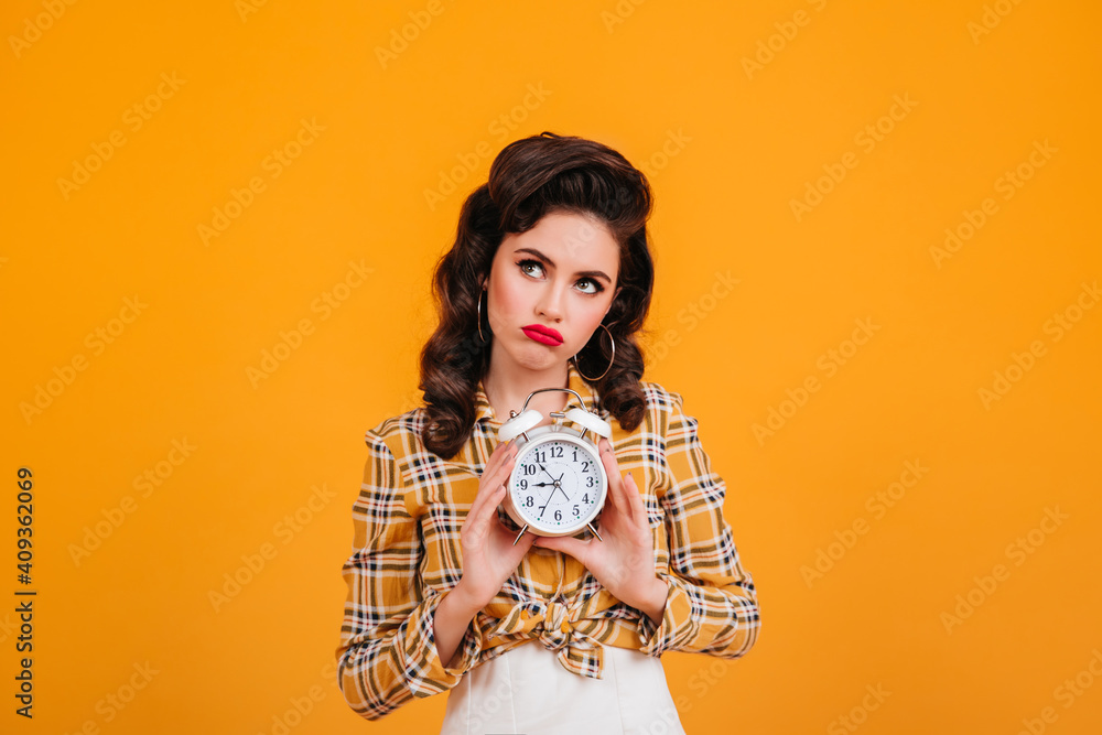 Sad pinup girl holding clock. Studio shot of pensive young woman in yellow checkered shirt. Sad pinup girl holding clock. Studio shot of pensive young woman in yellow checkered shirt.