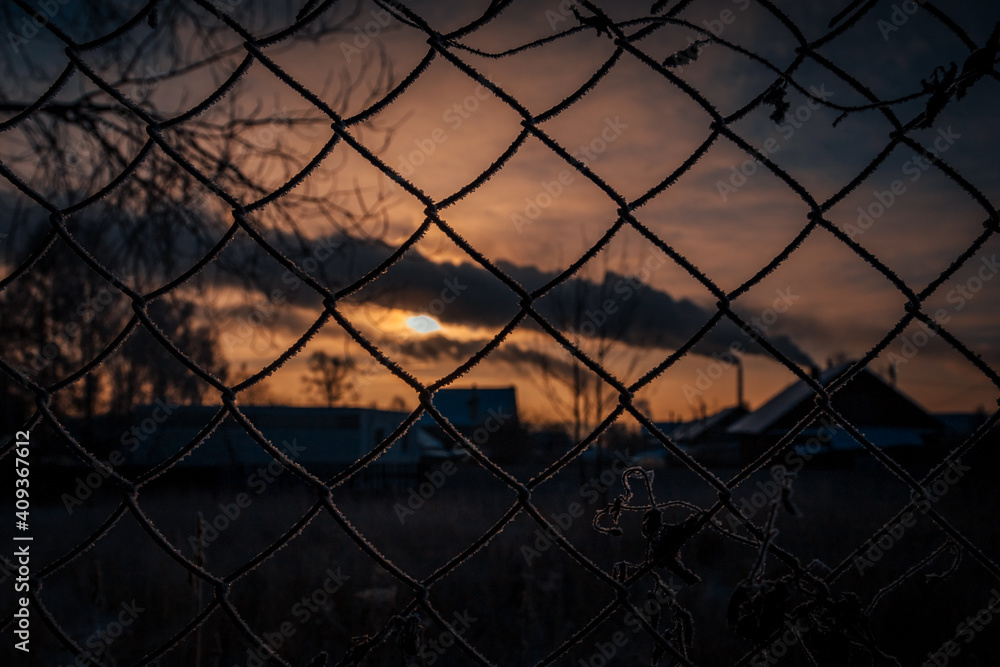 a bright disc of the sun peeps through the clouds against the background of a lattice of metal mesh on the fence a bright disc of the sun peeps through the clouds against the background of a lattice of metal mesh on the fence