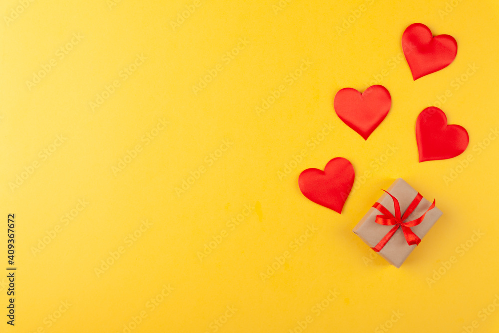 Gift box with ribbon and red hearts on yellow colored background, valentine's day greeting card