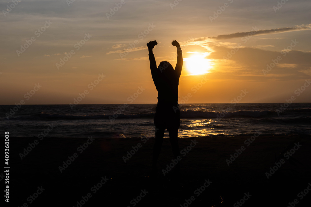 Beautiful woman silhouette showing joy with both hands raised In the sunrise at the sea in the morning of nature