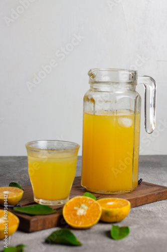 Es jeruk peras or orange juice iced with cut of sweet oranges. Served on clear glass on wooden rustic board. Grey grainy background. 