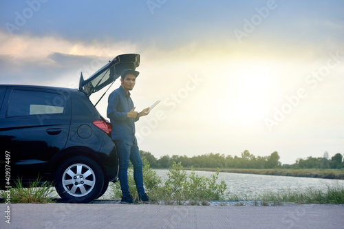 Asian man traveler use tablet sitting on hatchback car sunlight background