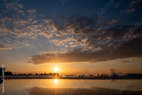 Foto View of sunset reflecting in a pool of water and an ocean wave crashing onto the