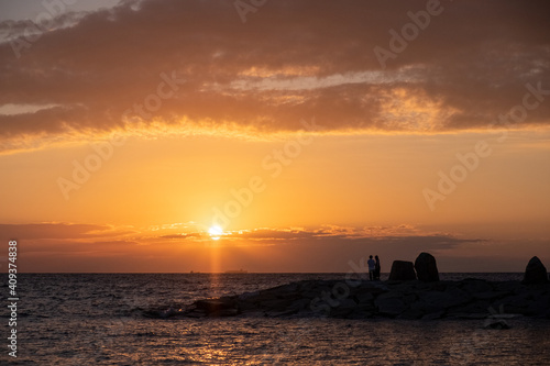 Cloudy sunset with silhouette of couple standing on a rocky shore at Shirahama Beach in Wakayama Prefecture, Japan