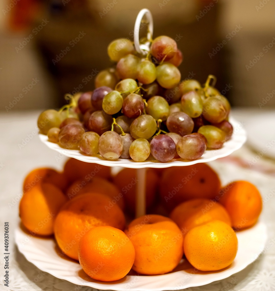 Grapes and tangerines on a two-tier white plate closeup Grapes and tangerines on a two-tier white plate closeup