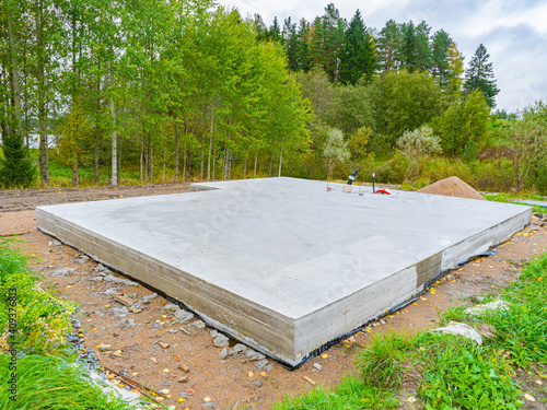 Concrete foundation next to trees. Construction near forest. Construction site with foundation. Foundation as a symbol of construction of a cottage. Building of a country cottage.