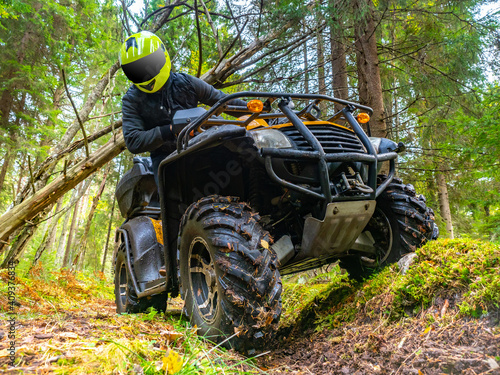 Portrait of a biker on an ATV. Biker rides in woods. He looks at wheels of quadbike. Biker on the background of the forest. ATV rider in green taiga. ATV as a symbol of extreme sports.