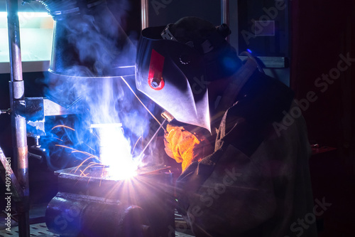 Portrait of a welder at work. A man with a welding machine in the dark. A man in a welding mask with his back to the camera. It works hot welder. Welder metal with arc welding machine