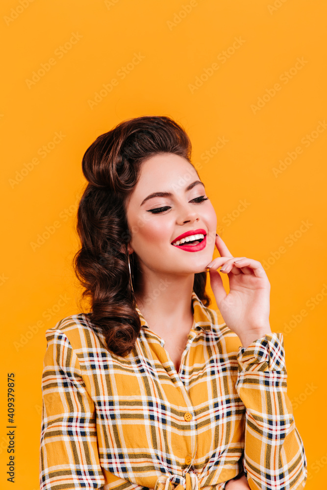 Sensual young woman with wavy hairstyle posing on yellow background. Studio shot of playful pinup girl in vintage checkered shirt. Sensual young woman with wavy hairstyle posing on yellow background. Studio shot of playful pinup girl in vintage checkered shirt.