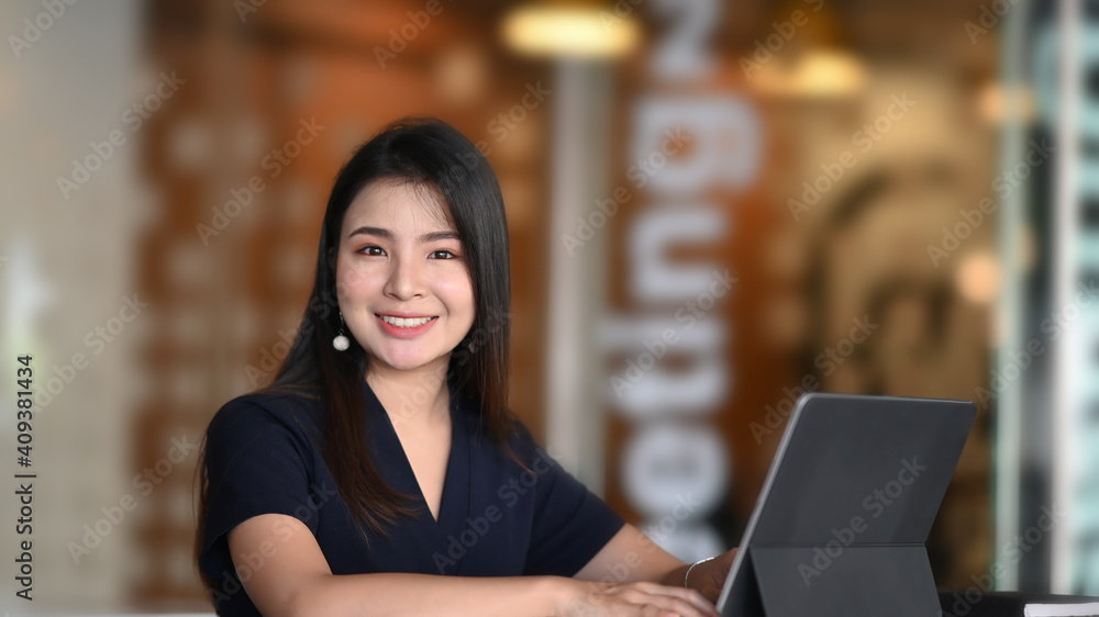 Smiling young female entrepreneur working on tablet computer and smiling to camera. Smiling young female entrepreneur working on tablet computer and smiling to camera.