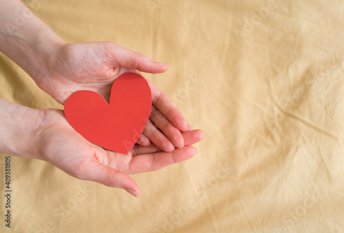 Beautiful paper heart-valentine in open hands against the background of yellow fabric. February 14