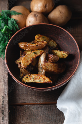 Delicious baked country potatoes in a earthen bowl with spices, dill and green onions, on a wooden table