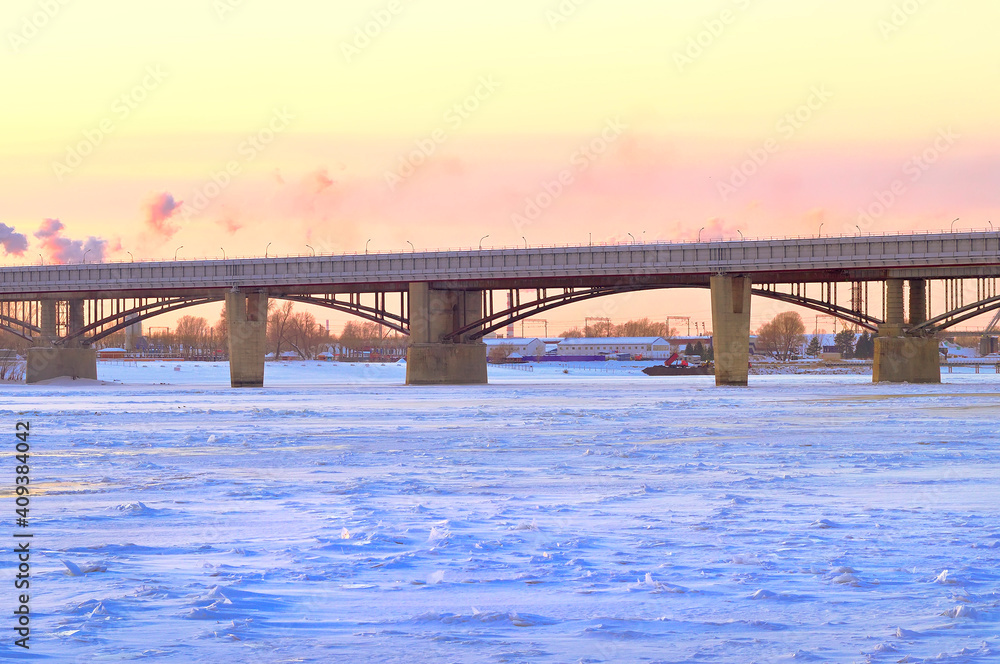 Winter evening on the Ob. The municipal and metro bridges cross a wide river, covered with ice