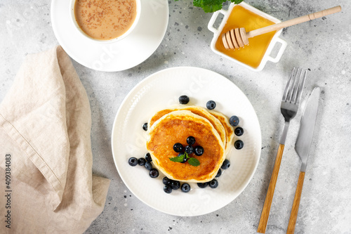 Pancakes in a white plate on the light gray kitchen table. Homemade delicious pancakes with honey and blueberries. Delicious sweet and hearty breakfast 