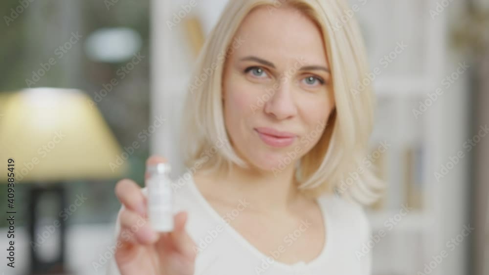 Rack focus, headshot of beautiful slim Caucasian woman smiling at camera holding Covid-19 vaccine in hand. Confident young lady posing with vaccination flask indoors. Slow motion. Rack focus, headshot of beautiful slim Caucasian woman smiling at camera holding Covid-19 vaccine in hand. Confident young lady posing with vaccination flask indoors. Slow motion.
