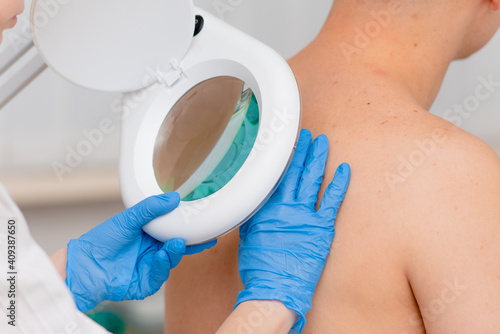 Fotografie A dermatologist examines the skin on the body of a young man through a magnifying glass of a cosmetology lamp