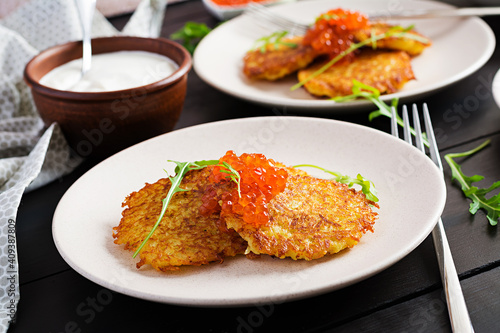 Fried potato pancakes with red caviar and sour cream, fritter, roesti. Traditional delicious food, lunch.