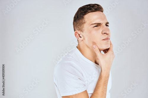Emotional man in a white t-shirt holds his hand on his face light background