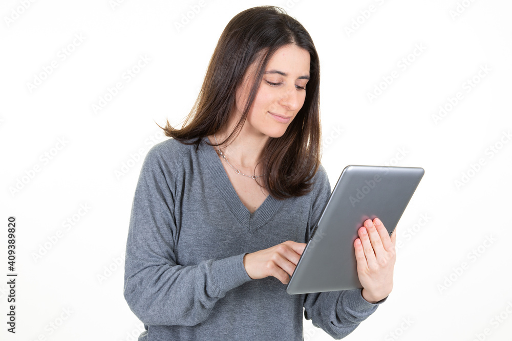 Portrait of adorable smiling woman with long brown hair holding and looking at tablet computer isolated over white background in studio Portrait of adorable smiling woman with long brown hair holding and looking at tablet computer isolated over white background in studio