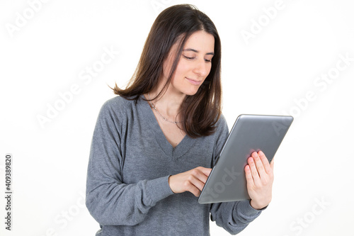 Portrait of adorable smiling woman with long brown hair holding and looking at tablet computer isolated over white background in studio