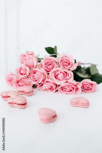 Pink roses on a white surface with pink heart shaped macaroons for anniversary