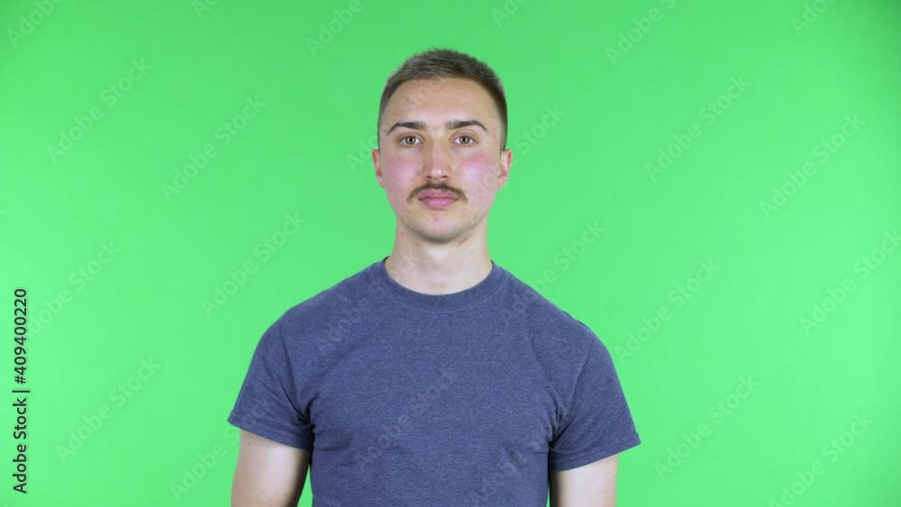 Portrait of a young man with TV remote in her hand, switching on TV and very laughs, scared and then upset. Cute male with a mustache in a blue t-shirt posing on a green screen in the studio. Close up Portrait of a young man with TV remote in her hand, switching on TV and very laughs, scared and then upset. Cute male with a mustache in a blue t-shirt posing on a green screen in the studio. Close up