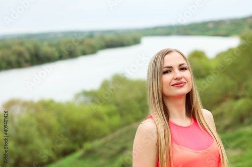 Portrait of the beautiful long haired blonde woman posing in front of the river bank. Focus on the right side. Woman spending time outdoors by the nature. 