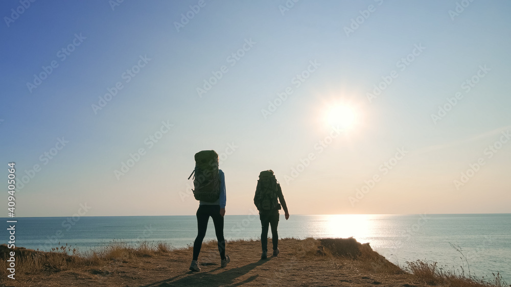 The couple with backpacks walking on a mountain against the sea sunset